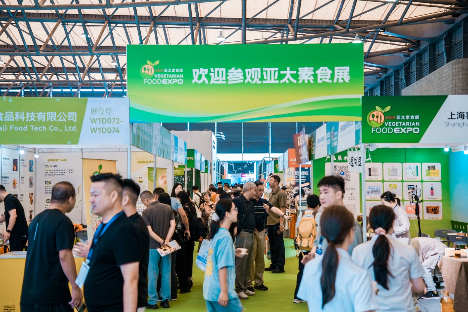 Visitors walking between exhibition booths beneath a green vegetarian food exhibition sign.